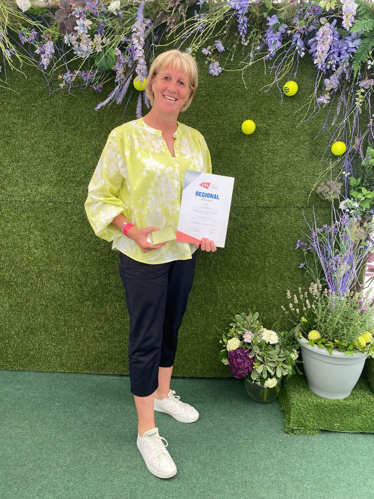 Sue standing holding the Glass Trophy and Regional Certificate dressed in a summer yellow blouse