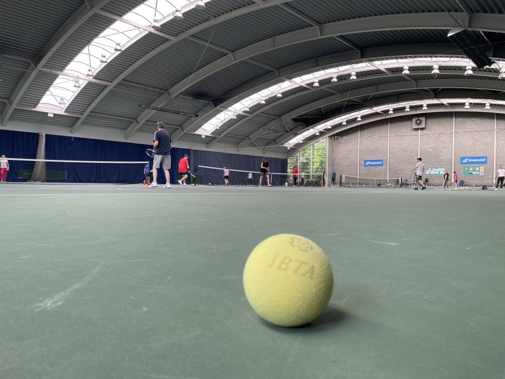 IBTA Sound Tennis Ball in the foreground with tennis courts in the background