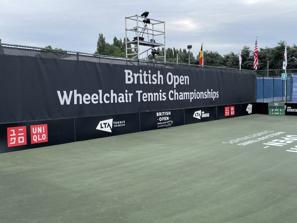 British Open Wheelchair Tennis Championships Banner behind the court, with a scaffold camera base for filming behind the court