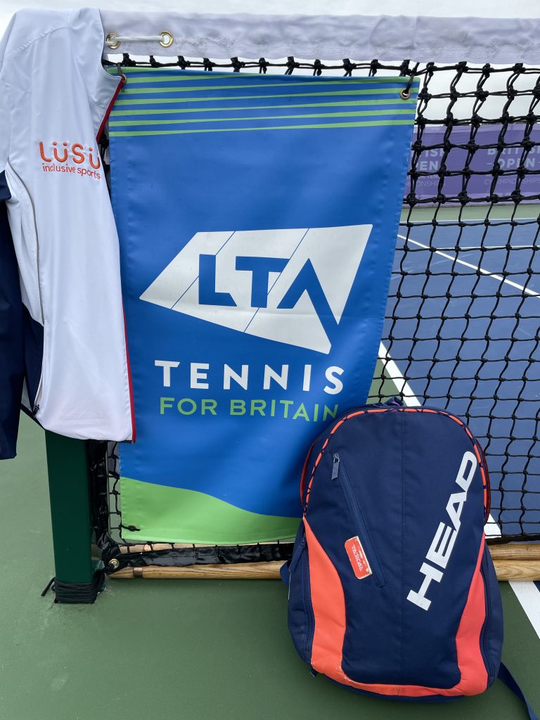 LUSU Tracksuit on the net post, with the LTA banner on the net, and a Head rucksack resting against the net