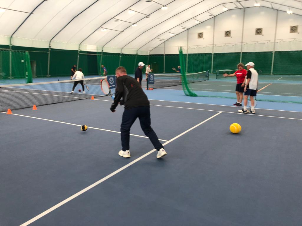 Coaches working in small groups on the tennis court, using rackets and lightweight balls