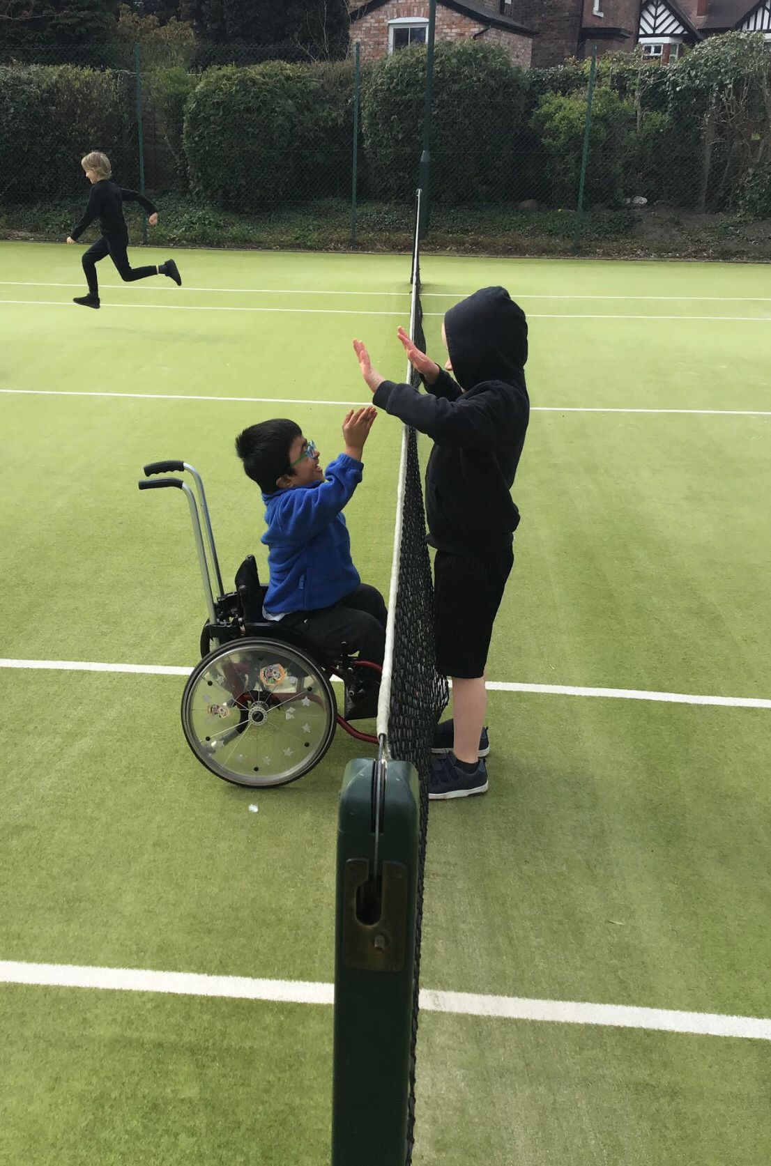2 children at the net high fiving, one child is a wheelchair user